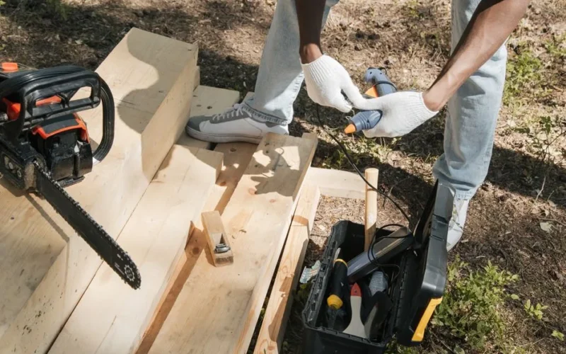 A carpenter using power tools to work on a wooden panel outdoors, showcasing construction and craftsmanship.