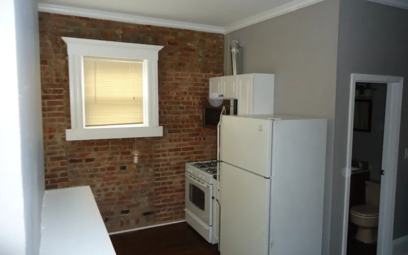 Kitchen renovation project finished. View of exposed brick wall, stove and microwave, painted walls, moldings, new floor, new ceiling.