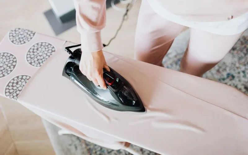 A person using a steam iron on a pink ironing board indoors, focusing on household chores.