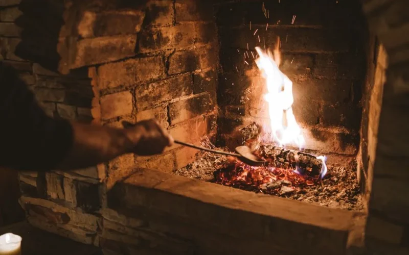A warm and inviting fireplace with flames dancing on logs in a brick surround, perfect for winter comfort.