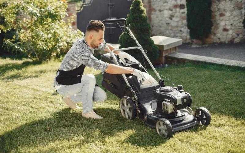 Man in summer attire using a lawnmower on a sunny day, showcasing gardening tools.