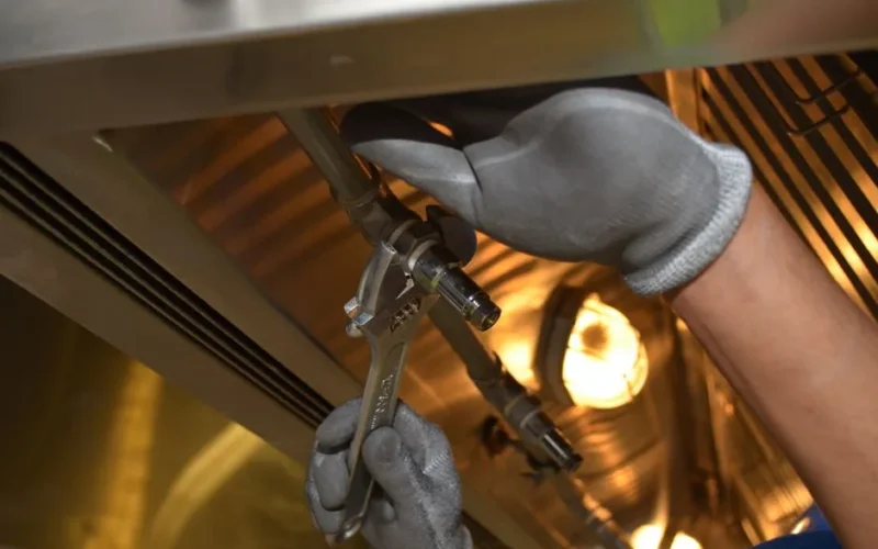 A worker fixing pipes with tools in an industrial indoor environment.